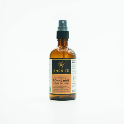 Sur fond blanc, Bouteille de 100ml en verre ambré avec spray, étiquette orangée contenat une lotion biphasée pour nourrir, hydrater et protéger la peau